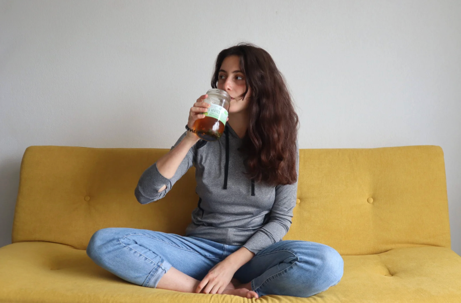 Sara assise sur un canapé jaune, avec une infusion dans la main