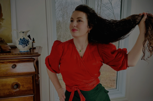 Katherine tenant ses cheveux longs dans une main. Elle porte des vêtements de style ancien.