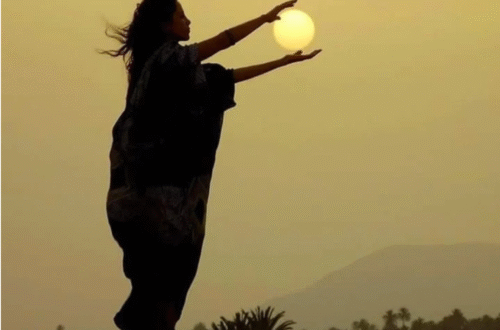 Nathalie, dans le desert, ses mains entourant le soleil que l'on voit au loin dans le ciel.