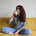 Sara assise sur un canapé jaune, avec une infusion dans la main